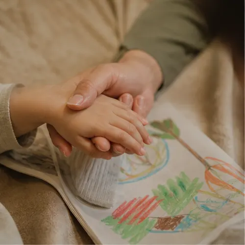 Parent hand holding child hand near a drawing